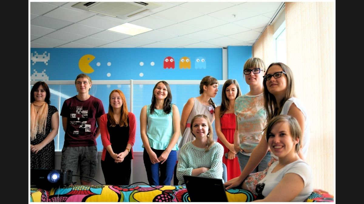 Group photo of a cheerful team in a colorful office with a Pac-Man mural in the background.